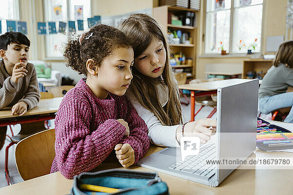 Schoolgirls sharing laptop together at desk in classroom
