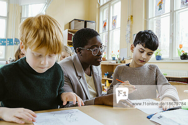 Lehrer hilft Jungen beim Lösen von Problemen  während sie am Schreibtisch im Klassenzimmer sitzen