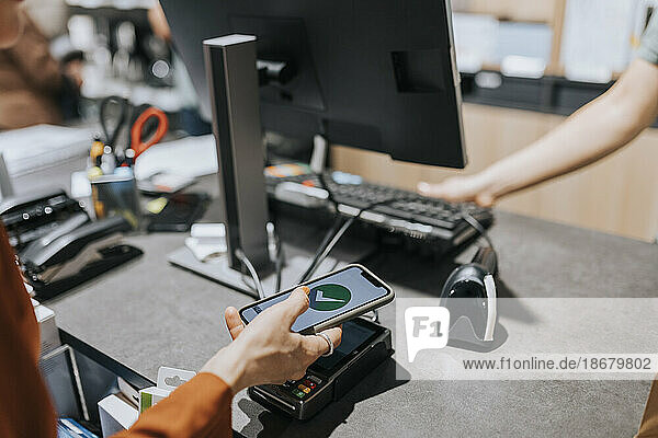 Ausgeschnittenes Bild eines Kunden  der ein Kreditkartenlesegerät scannt  während er mit seinem Smartphone in einem Elektronikgeschäft bezahlt