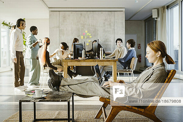 Seitenansicht einer Geschäftsfrau  die einen Laptop benutzt  während sie auf einem Stuhl im Kreativbüro sitzt