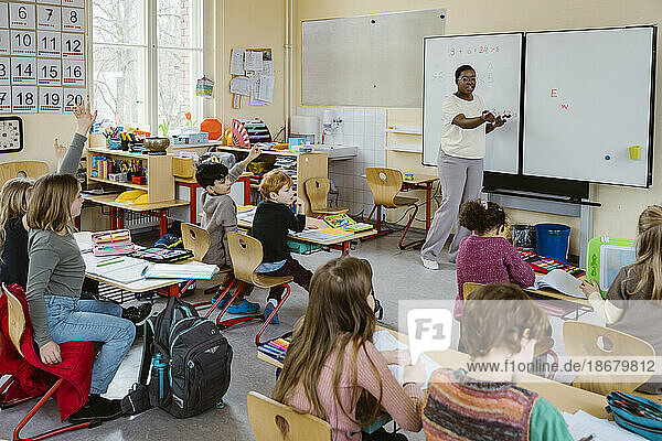 Lehrerin im Gespräch mit männlichen und weiblichen Schülern während einer Vorlesung im Klassenzimmer