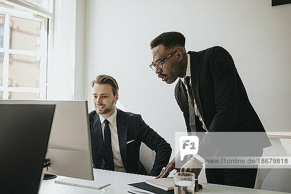 Männliche Unternehmer  die am Schreibtisch im Büro über einen Desktop-PC diskutieren