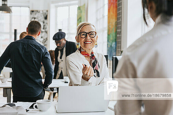 Happy businesswoman wearing eyeglasses discussing with colleague at office