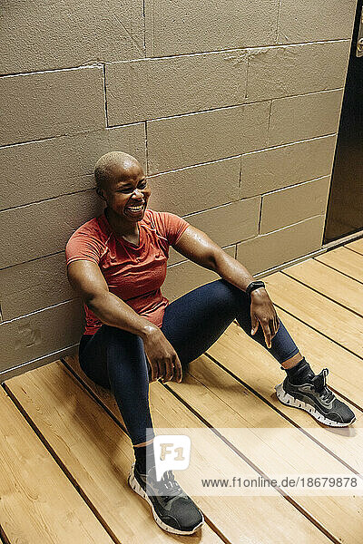 Glückliche Sportlerin macht Pause  während sie im Fitnessstudio auf dem Boden sitzt