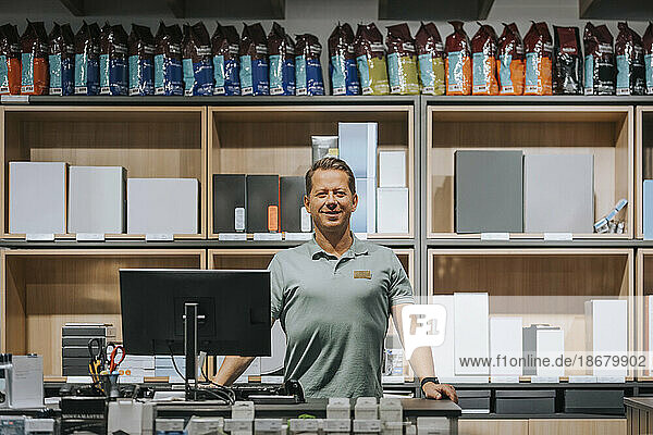 Portrait of confident mature salesman standing at checkout counter in appliances store