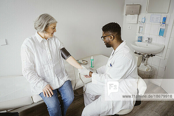 Young male doctor checking blood pressure of female patient at clinic