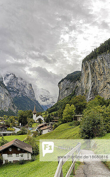 Path among green meadows of the alpine village of Lauterbrunnen with Trummelbach Falls in the background  Bern canton  Switzerland  Europe