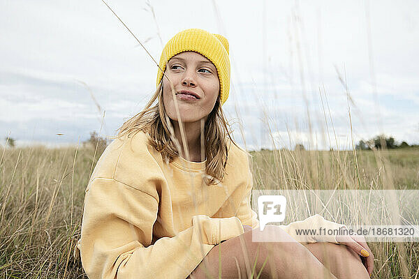 Smiling girl (10-11) in yellow beanie sitting in grass
