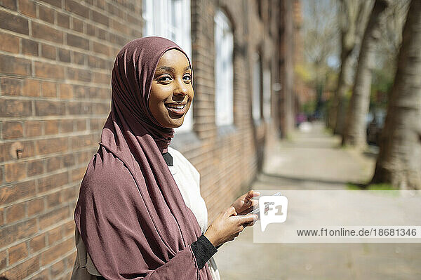 Young woman wearing hijab using phone in street