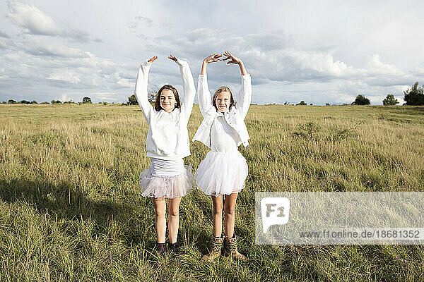 Smiling girl friends (10-11) doing ballet pose in field