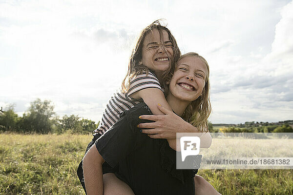 Smiling girl (10-11) giving friend piggyback ride