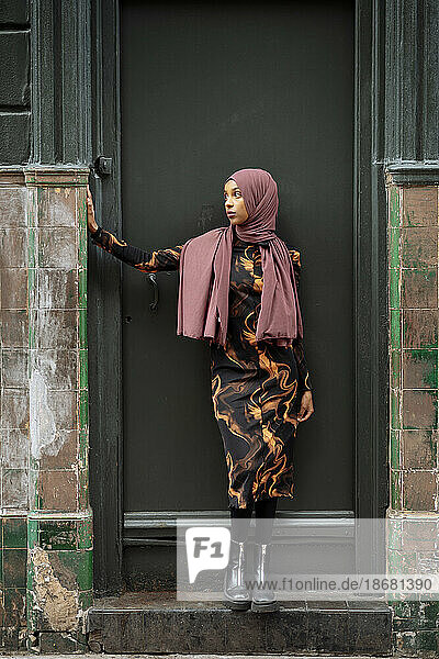 Young woman in hijab standing in front of run-down building