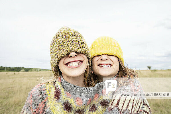 Smiling girl friends (10-11) wearing beanies over eyes