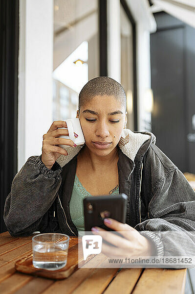 Hipster young woman drinking coffee and using phone in cafe