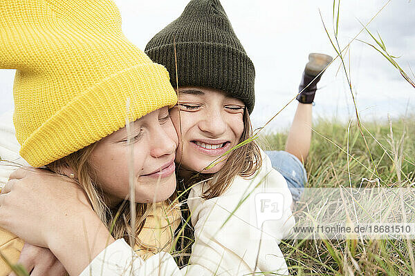 Smiling girl friends (10-11) lying in grass and hugging