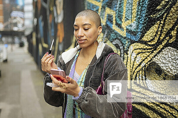 Hipster young woman applying lip gloss in street