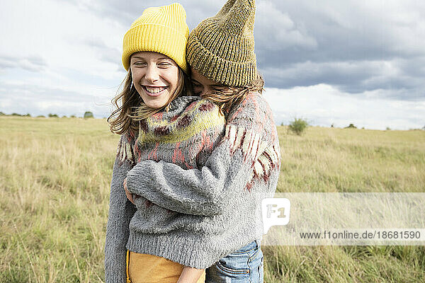 Smiling girl friends (10-11) wearing one sweater in field and hugging