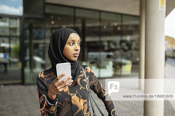 Young woman in hijab using phone in city