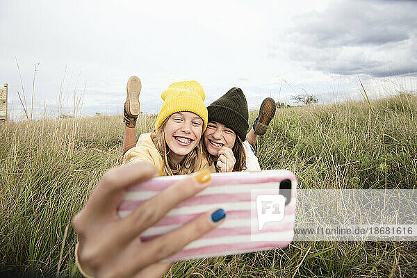 Smiling girl friends (10-11) lying in grass and taking selfie
