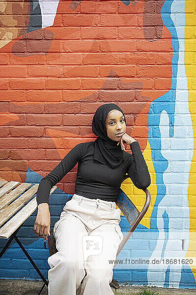 Young woman wearing hijab sitting against mural