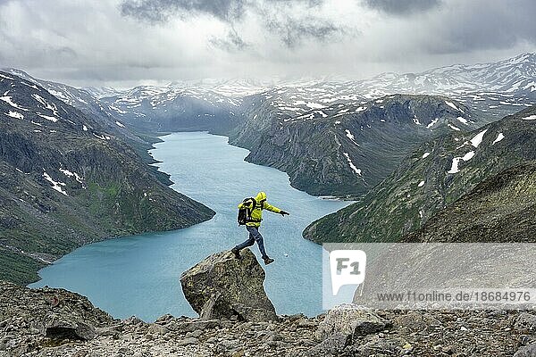 Bergsteiger springt von Felsen  Besseggen Wanderung  Gratwanderung  Ausblick auf See Gjende und verschneite Berge  Jotunheimen Nationalpark  Vågå  Innlandet  Norwegen  Europa