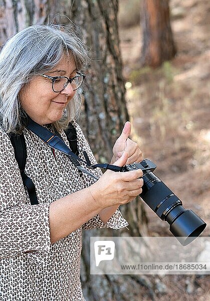 Weißhaarige  bebrillte Fotografin lächelt  während sie die Fotos auf ihrer Kamera mit einem zustimmenden Nicken betrachtet