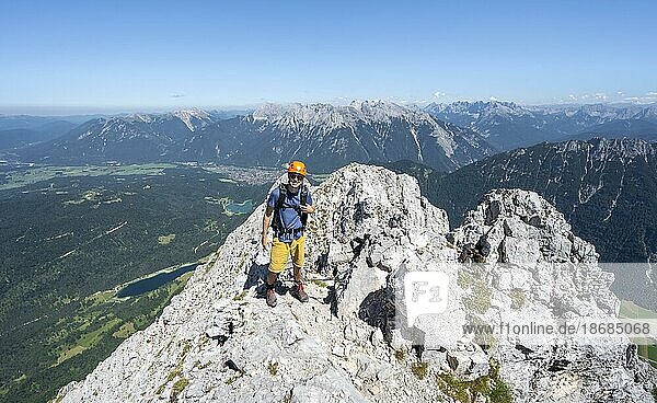 Bergsteiger klettert im Fels  beim Aufstieg zur Oberen Wettersteinspitze  hinten Gipfel des Karwendelgebirge  Wettersteingebirge  Bayerische Alpen  Bayern  Deutschland  Europa