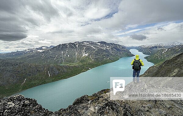 Bergsteiger blickt in die Ferne  Besseggen Wanderung  Gratwanderung  Ausblick auf See Gjende und verschneite Berge  Jotunheimen Nationalpark  Vågå  Innlandet  Norwegen  Europa