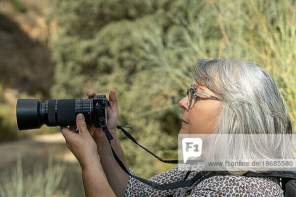 Ältere Fotografin mit weißen Haaren und Brille  die ein Foto macht und durch den Sucher ihrer Kamera schaut