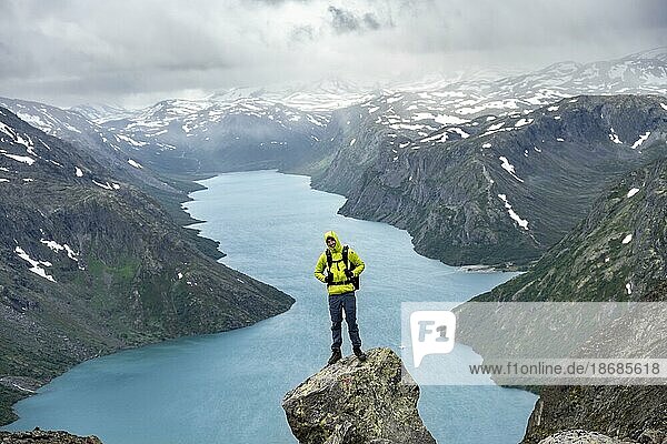 Bergsteiger steht auf Felsen  Besseggen Wanderung  Gratwanderung  Ausblick auf See Gjende und verschneite Berge  Jotunheimen Nationalpark  Vågå  Innlandet  Norwegen  Europa