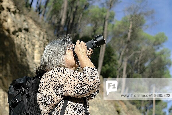 Fotografin im Profil und Rucksack beim Fotografieren mit ihrer Kamera im Wald