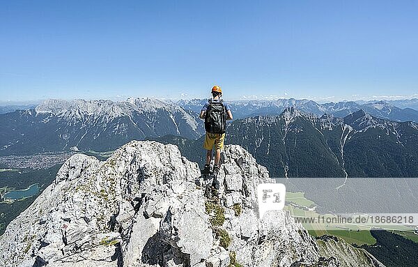 Bergsteiger klettert im Fels  beim Aufstieg zur Oberen Wettersteinspitze  hinten Gipfel des Karwendelgebirge  Wettersteingebirge  Bayerische Alpen  Bayern  Deutschland  Europa