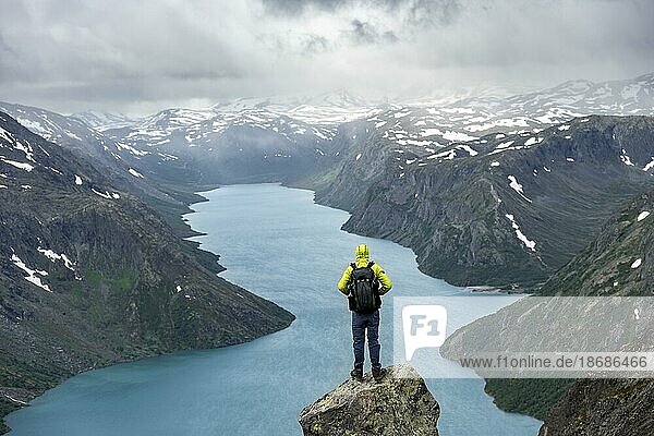 Bergsteiger steht auf Felsen  Besseggen Wanderung  Gratwanderung  Ausblick auf See Gjende und verschneite Berge  Jotunheimen Nationalpark  Vågå  Innlandet  Norwegen  Europa