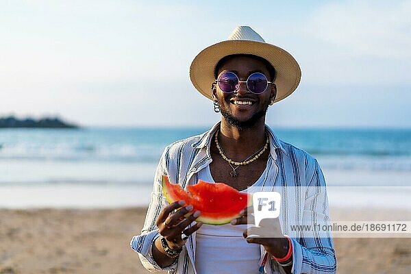 Porträt eines schwarzen ethnischen Mannes genießen Sommerurlaub am Strand essen eine Wassermelone am Meer