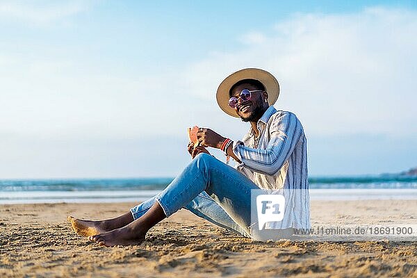 Portrait of a black ethnic man enjoy summer vacation at the beach eating a watermelon  Sitting on the sand