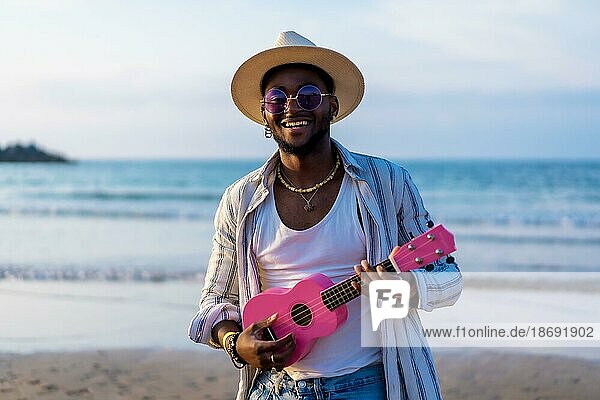 Porträt von schwarzen ethnischen Mann genießen Sommerurlaub am Strand spielen Ukulele