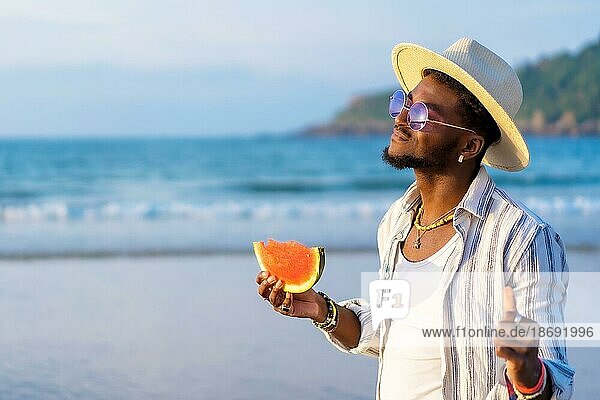 Portrait of a black ethnic man enjoy the summer vacation on the beach eating a watermelon  enjoying the freedom