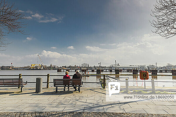 Seniorenpaar sitzt auf Bank in der Sonne und schaut auf den Nord-Ostseekanal an der Schleuse in Brunsbüttel