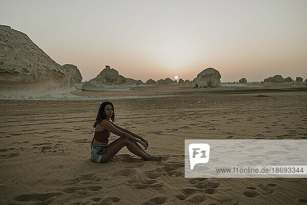 Frau sitzt bei Sonnenuntergang auf Sand in der Wüste
