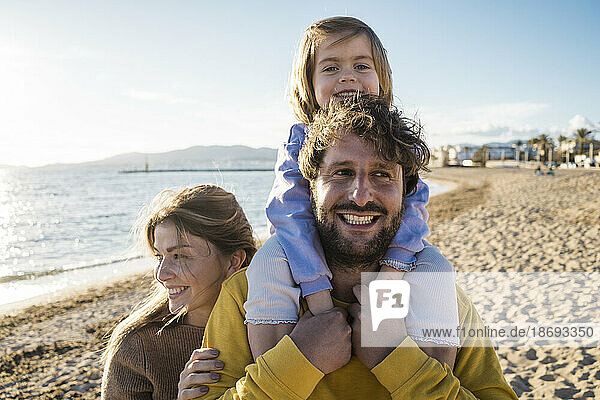 Cute girl sitting on father's shoulders by woman at beach