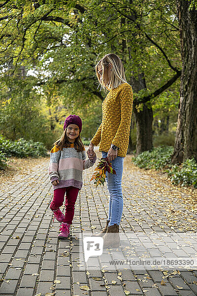 Smiling daughter holding mother's hand on footpath