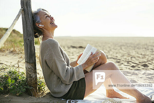 Happy mature woman with book sitting at beach