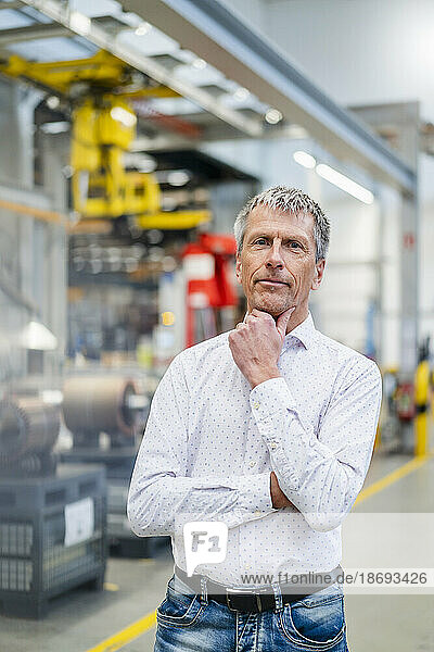 Businessman with hand on chin standing at factory