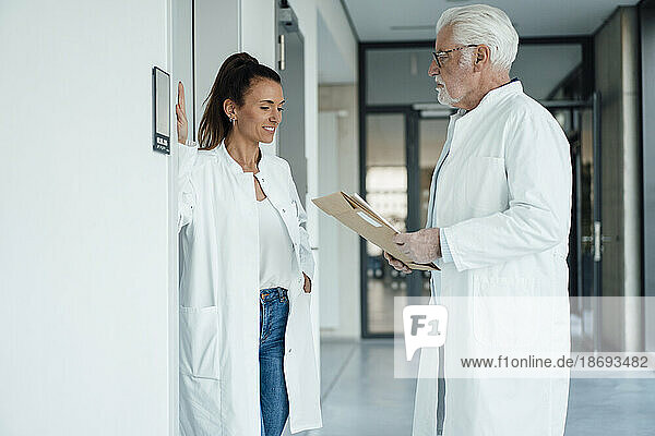 Smiling doctor discussing with senior colleague holding document in hospital
