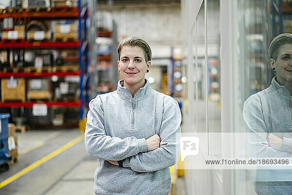 Smiling young employee with arms crossed standing in industry