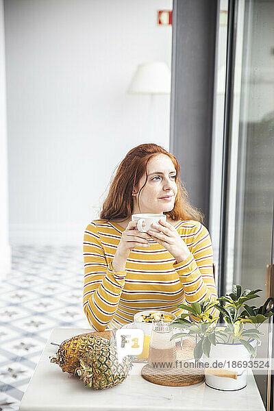 Frau hält Tasse und sitzt mit gesundem Frühstück am Tisch