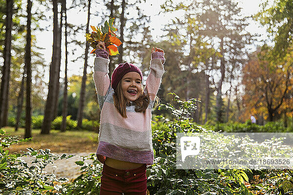 Fröhliches Mädchen  das im Park mit Blättern spielt