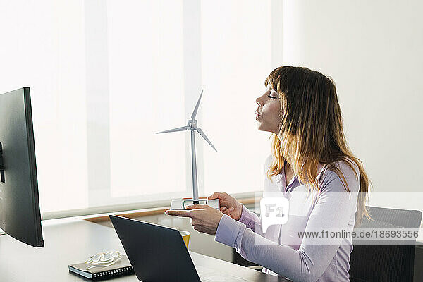 Businesswoman blowing on wind turbine model in office