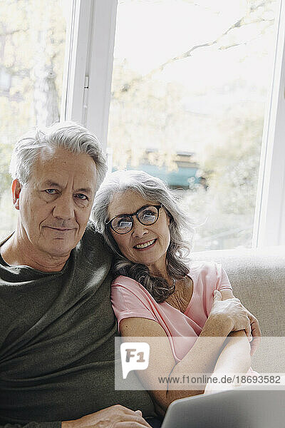 Portrait of senior couple with laptop relaxing on couch at home