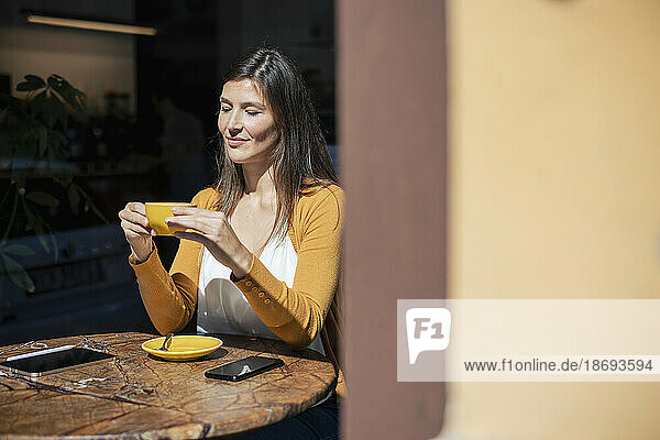 Woman holding coffee cup sitting at table in cafe